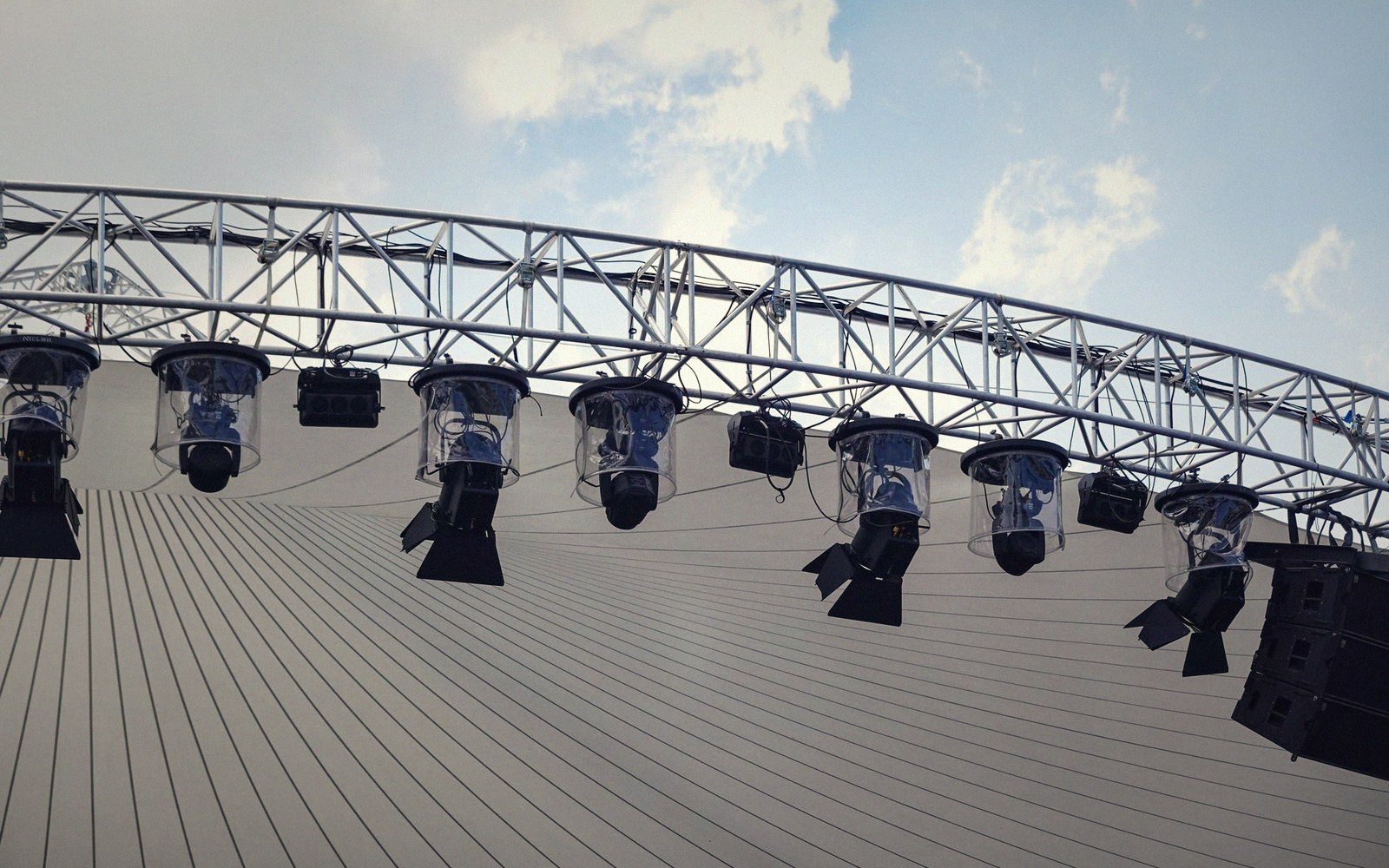 Stage lights and speakers hang from a curved truss above a tented venue roof