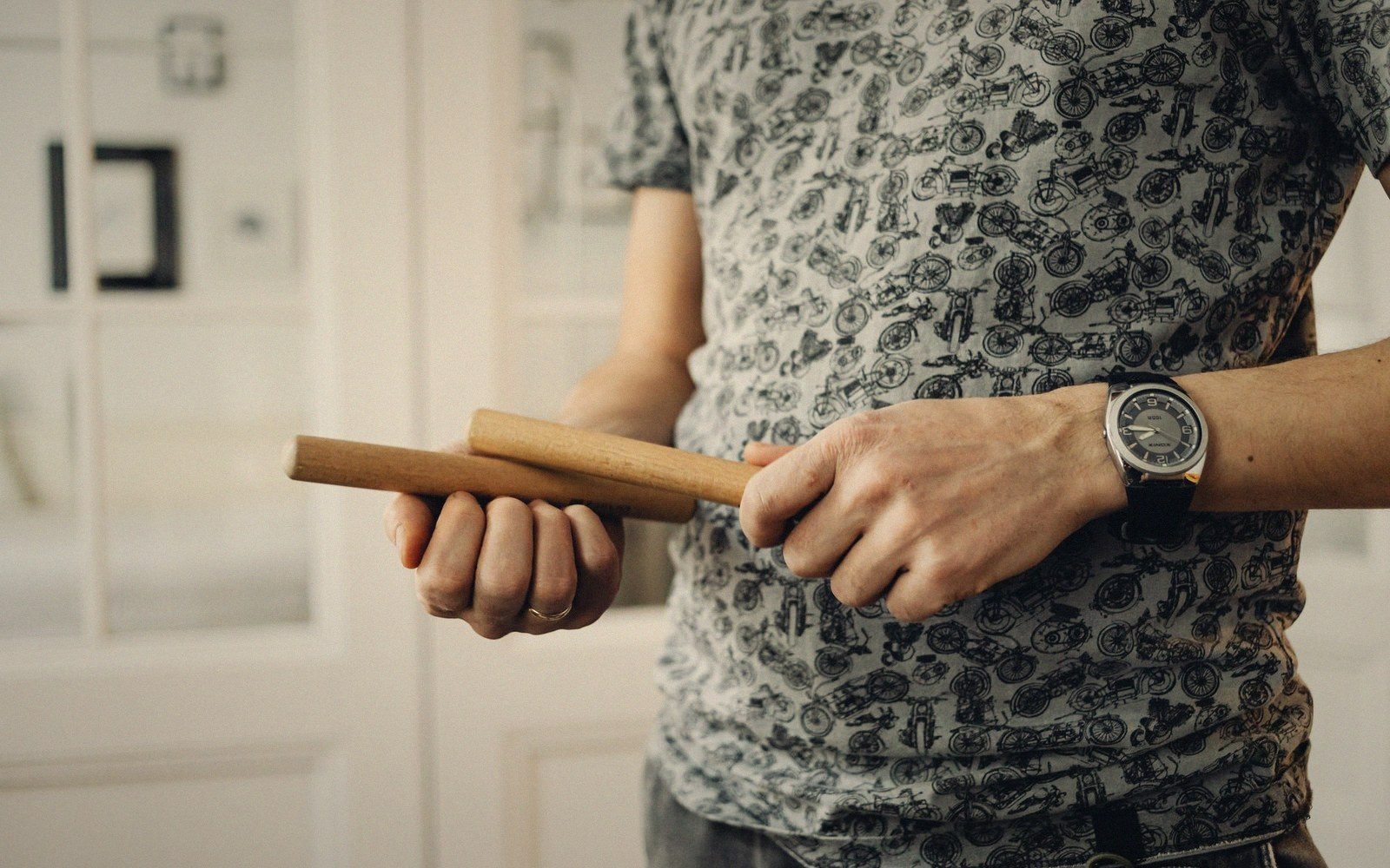 A man holds a pair of wooden claves while wearing a printed t-shirt and wristwatch
